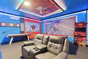 A room with a blue wall, a Spiderman-themed poster, a gaming table, and a leather chair. - Luxury 7BR Disney Home • Pool Spa • Game Room -  Resort Windsor Island (Four Corners)
