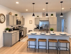 A modern kitchen with a central island, stainless steel appliances, and pendant lighting. - New 5BR Home . Walk to Dining . Sleeps 10 (Jacksonville)