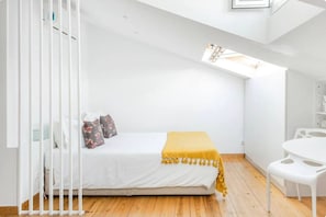 A small, white room with a bed, a yellow throw, and a white chair. - Skylight Mouraria Loft (Lisbon)