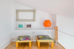 A room with two colorful stools, a framed picture, and a modern orange chair. - Skylight Mouraria Loft (Lisbon)