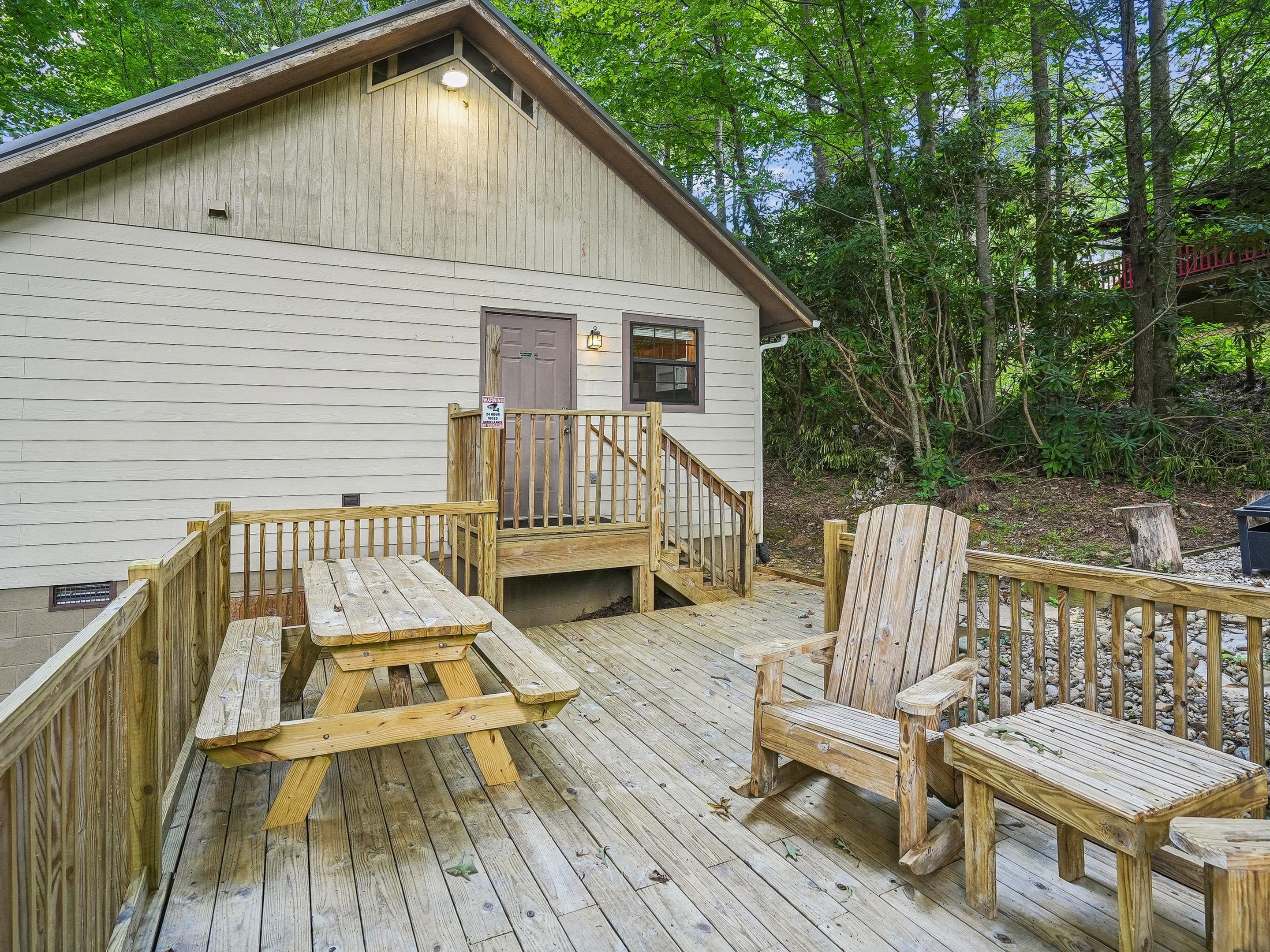 A wooden deck with picnic tables and chairs, a covered staircase, and a building with a door and windows.