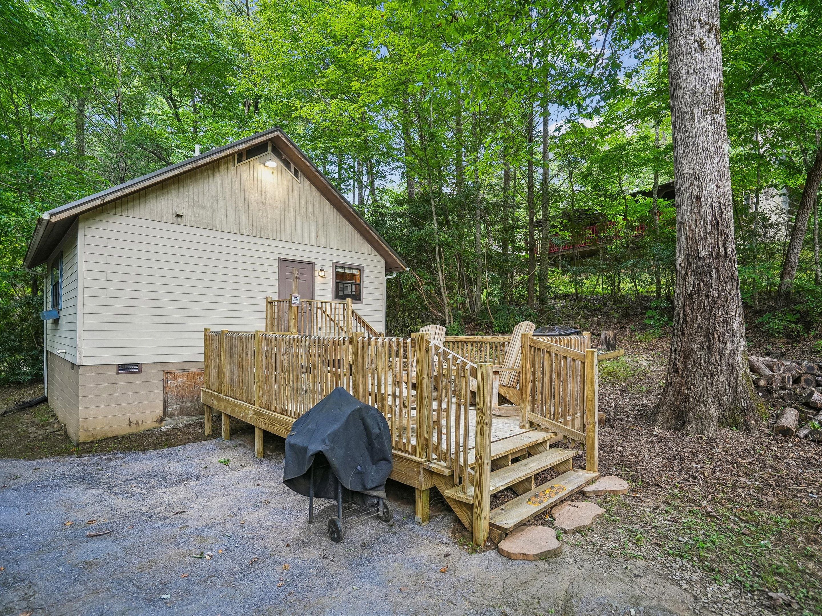 A wooden cabin with a porch and steps leading to a covered grill area.