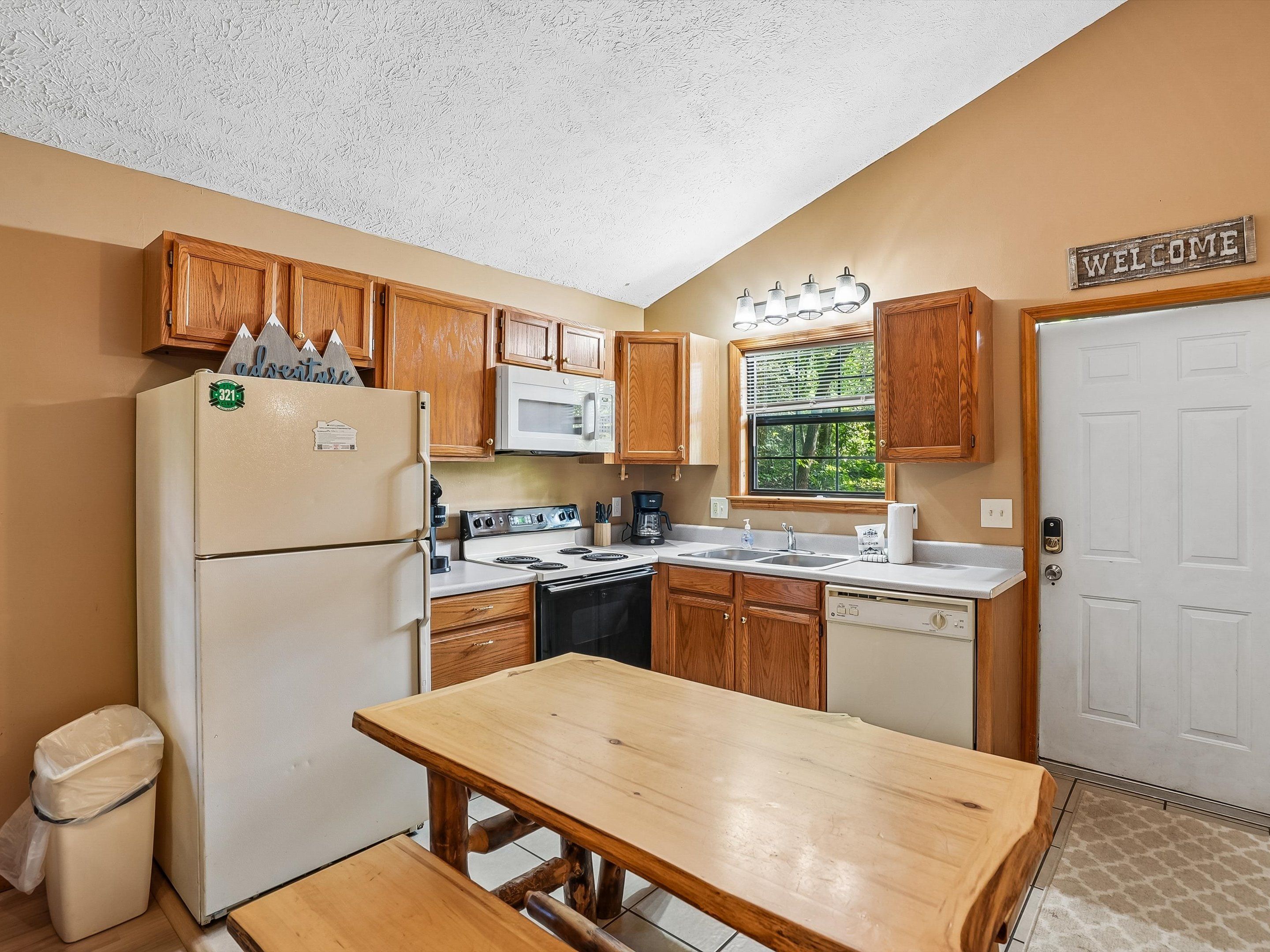 A compact kitchen with wooden cabinets, a white refrigerator, a microwave, a stove, and a sink.