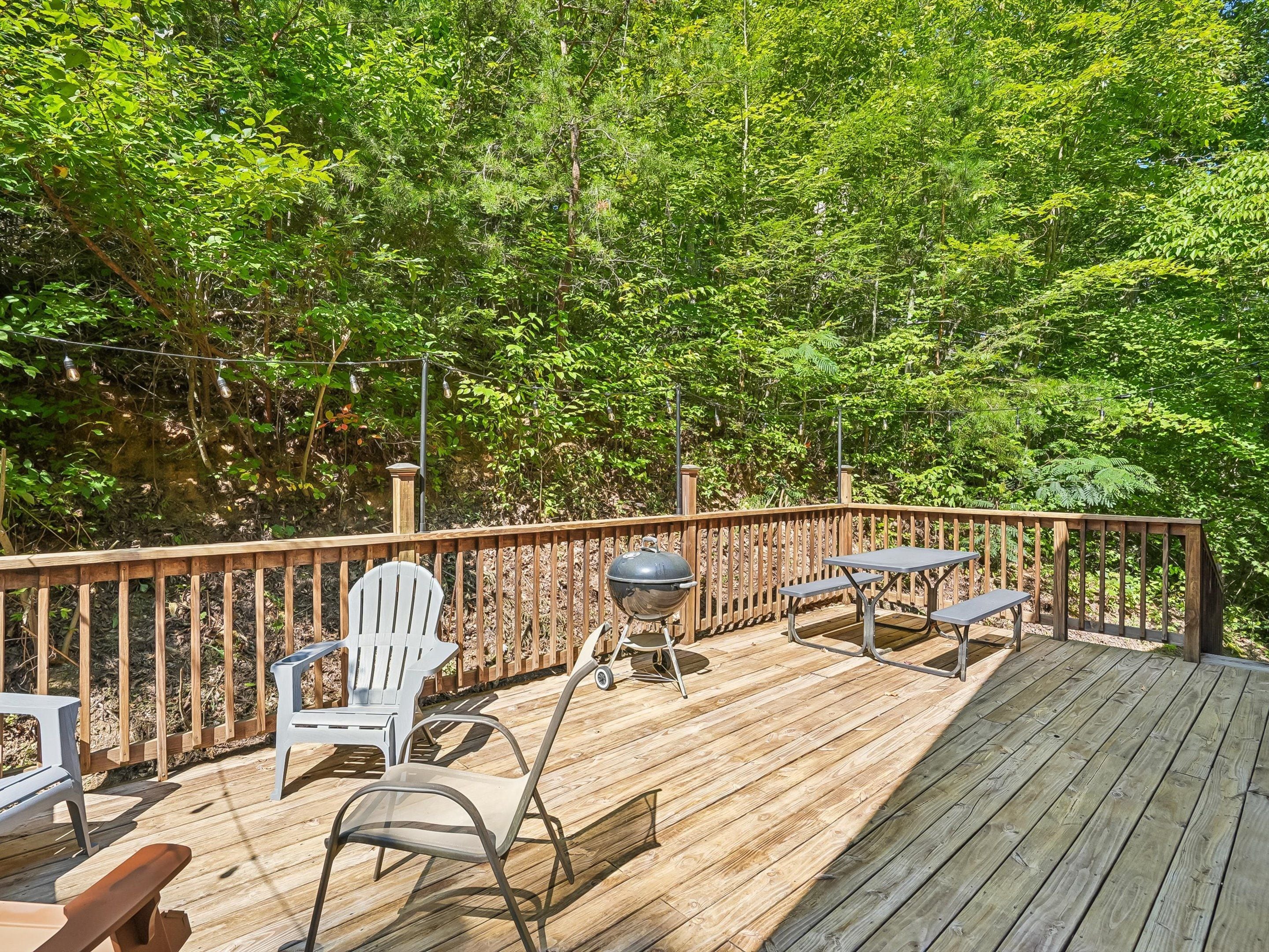 A wooden deck with outdoor furniture, including chairs and tables, surrounded by lush greenery.