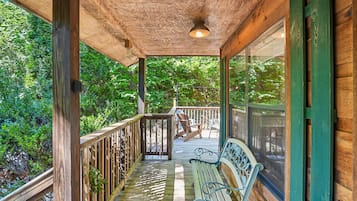 A wooden deck with a bench and railing, surrounded by greenery.