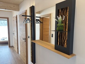 Un couloir avec un plancher en bois, un miroir à cadre noir et une étagère ornée d’une plante.