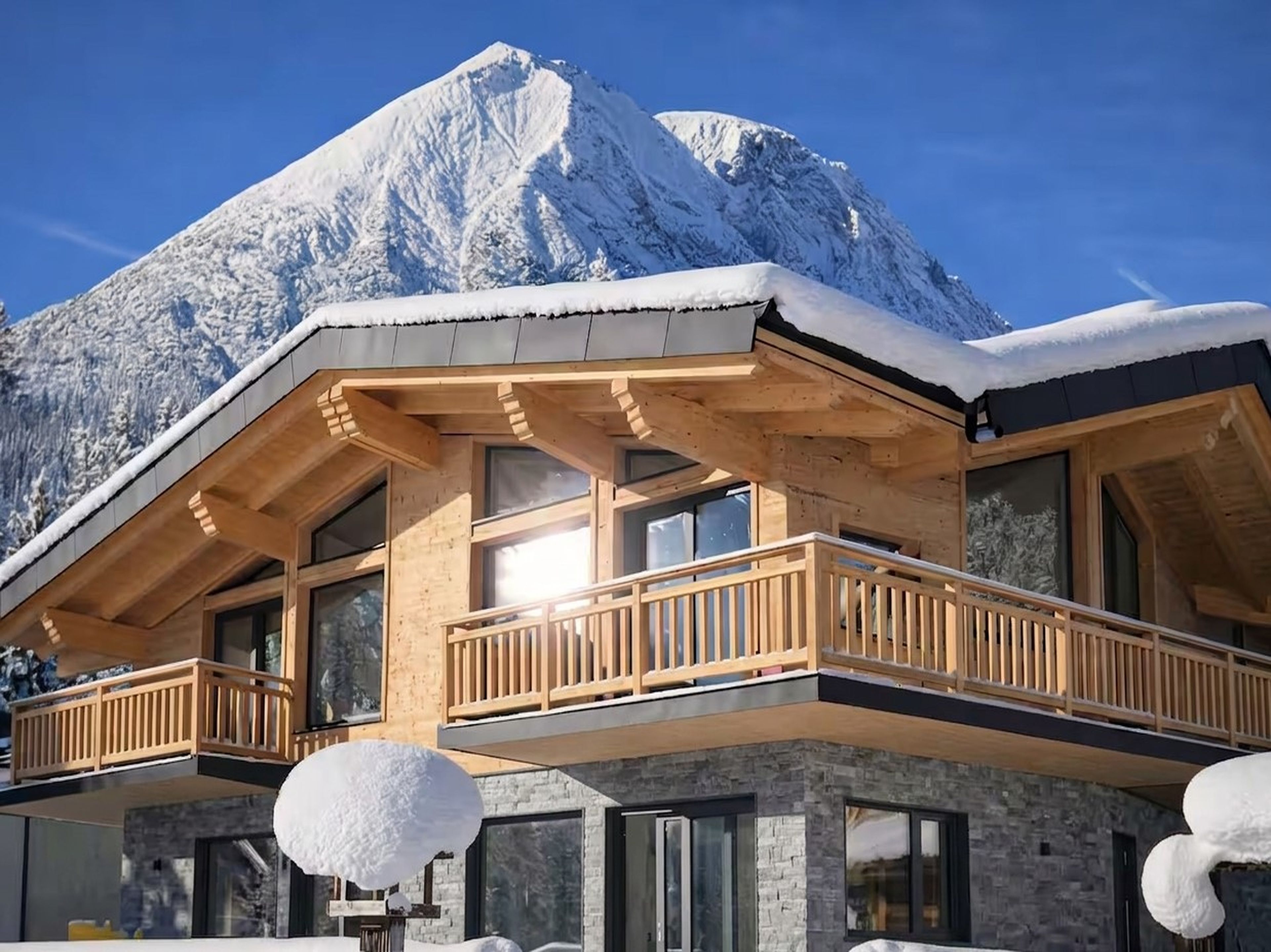 Un chalet en bois doté d’un balcon, de grandes fenêtres et surplombant un paysage montagneux.
