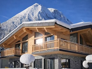 Un chalet en bois doté d’un balcon, de grandes fenêtres et surplombant un paysage montagneux.