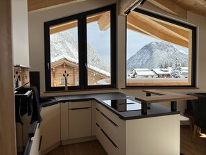Une cuisine moderne avec des meubles en bois et une grande fenêtre donnant sur un paysage montagneux enneigé.