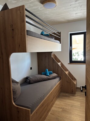 Un lit superposé avec une tête de lit en bois, un lit inférieur avec des oreillers et une fenêtre donnant sur un paysage verdoyant.