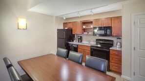 A compact kitchen with wooden cabinets, a black refrigerator, a microwave, a stove, and a dining table with chairs.