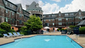 A swimming pool with lounge chairs, surrounded by brick buildings with a turret and multiple windows.