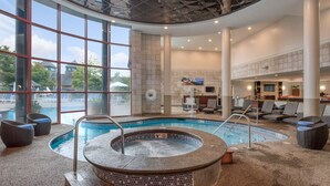 En stor indendørs swimmingpool med jacuzzi, liggestole og udsigt til det fri.