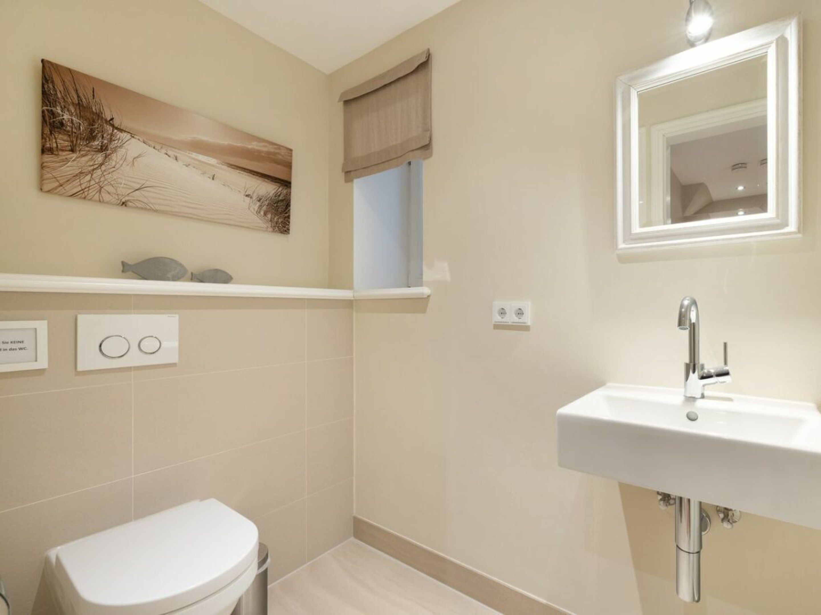 Une salle de bain comprenant des toilettes, un lavabo, un miroir et une étagère fixée au mur, décorée d’un motif de poisson.