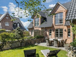 A brick house with a stone wall, a patio with outdoor furniture, and a clear sky. - Holiday Home in Sylt With 3 Bedrooms (Sylt)