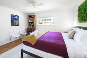 A bedroom with a bed, a ceiling fan, a bookshelf, two white chairs, a window with a view, and a wall-mounted plant. - South Austin Retreat: 10 Min Downtown + Yard (Austin)
