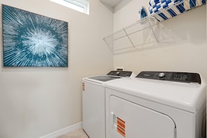 A laundry room with a front-loading washer and dryer, a window, and a wall-mounted shelf with towels. - Dream Family Escape, Pool and Themed Rooms (Clermont)