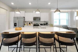 A modern kitchen with a central island, stainless steel appliances, and pendant lighting. - Dream Family Escape, Pool and Themed Rooms (Clermont)