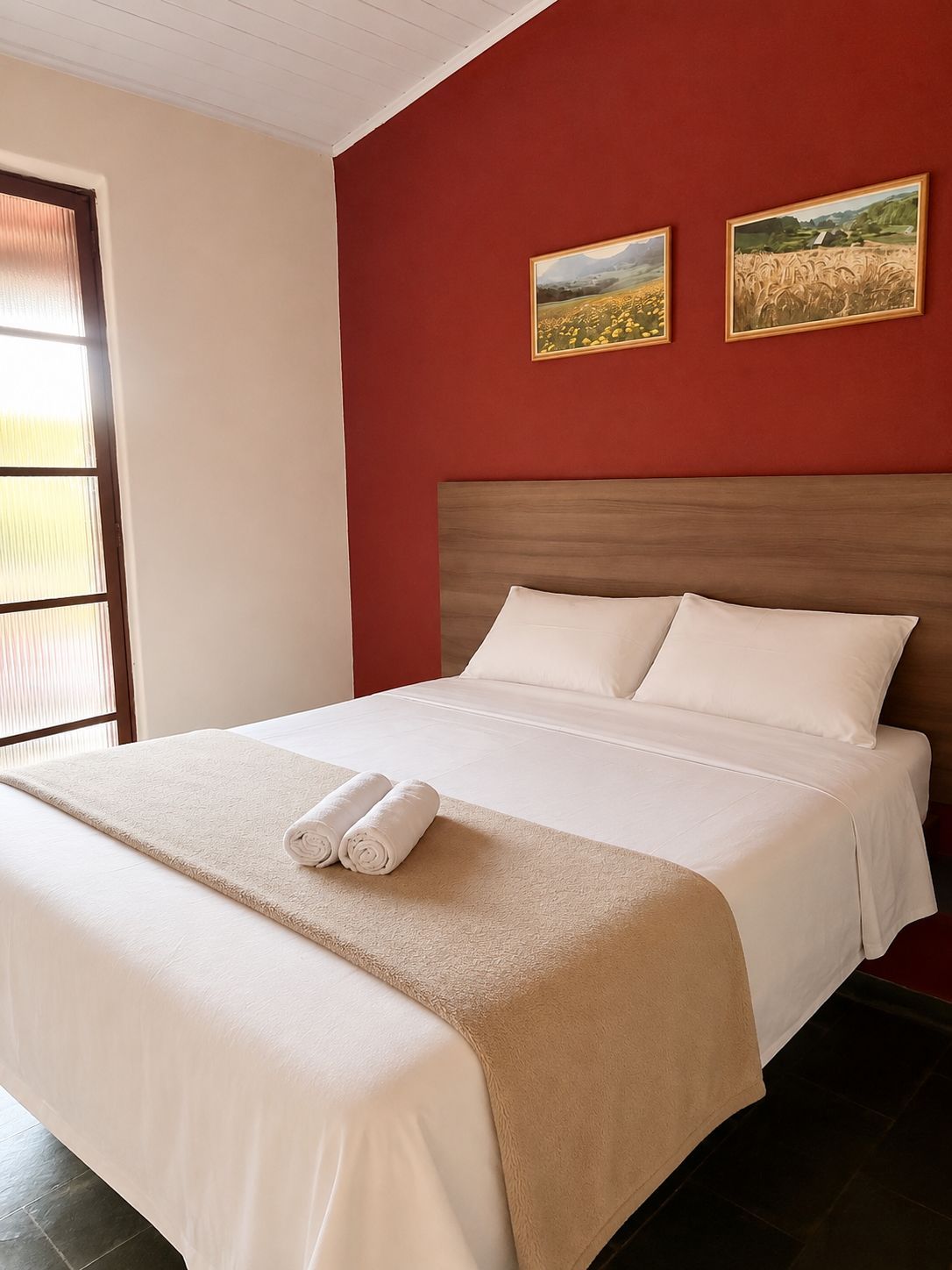 Une chambre d’hôtel avec un lit, deux tableaux accrochés au mur et une fenêtre avec des stores.