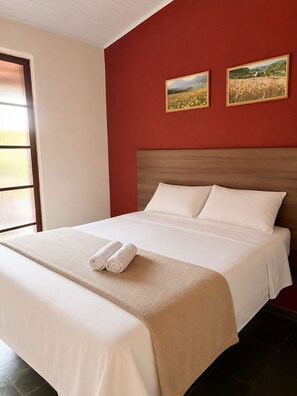 A hotel room with a bed, two paintings on the wall, and a window with blinds. - Pousada Sierra (Serra Negra)