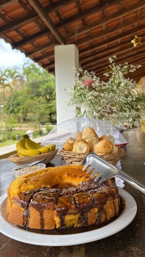 A dessert plate with a chocolate cake, a basket of bread rolls, and a bunch of bananas on a table. - Pousada Sierra (Serra Negra)