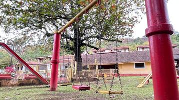 A playground with swings and a slide, surrounded by trees and buildings.
