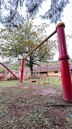 Un parque infantil con columpios y tobogán, rodeado de árboles y edificios.