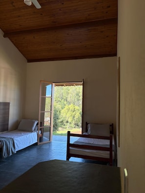 Una habitación con dos camas, techo de madera y un ventanal con vistas a árboles.