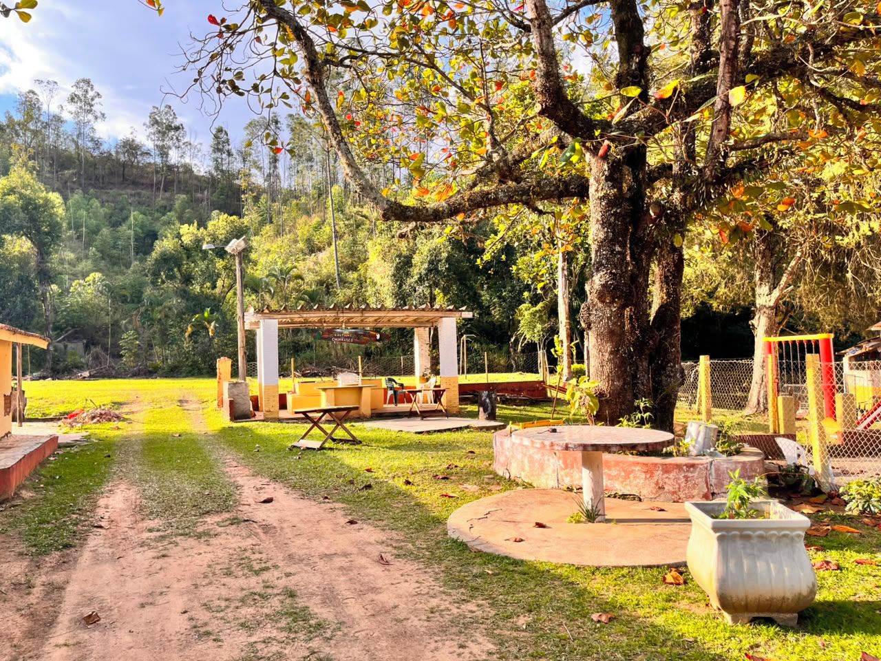 Un parc amb taules de pícnic, una zona coberta per seure i un camí de terra.