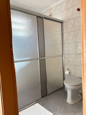 A bathroom with a toilet, a towel, and a shower enclosure. - Pousada Sierra (Serra Negra)