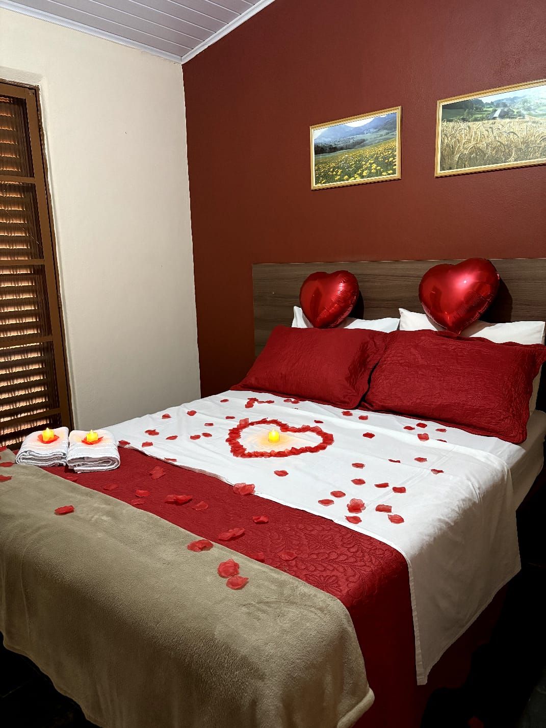 Ein Bett mit roter und weißer Bettwäsche, herzförmigen Kissen und einer herzförmigen Dekoration auf der Tagesdecke.
