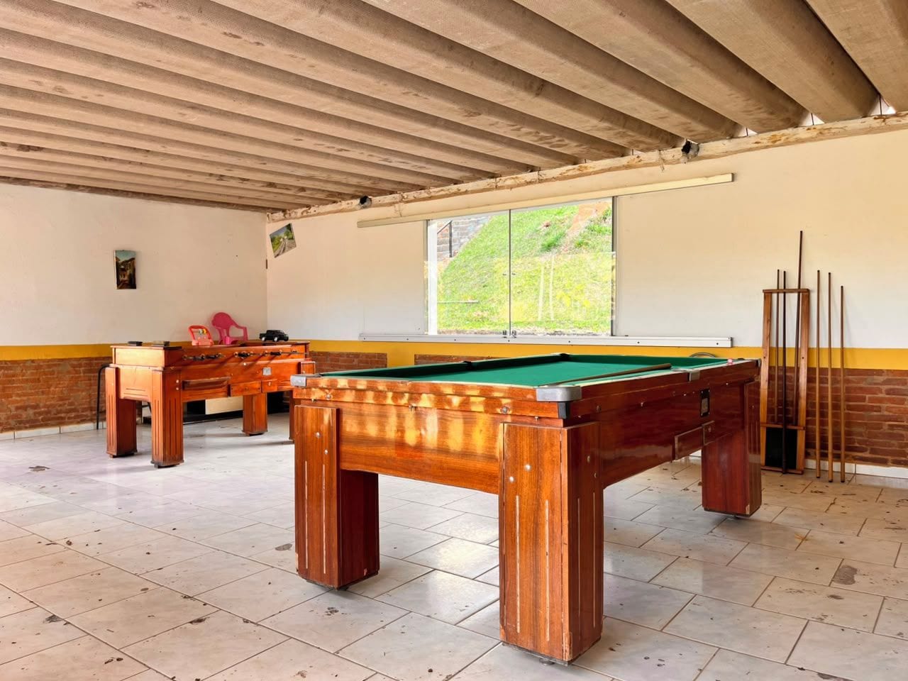 Une table de billard dans une pièce dont le sol est carrelé et qui possède une fenêtre.