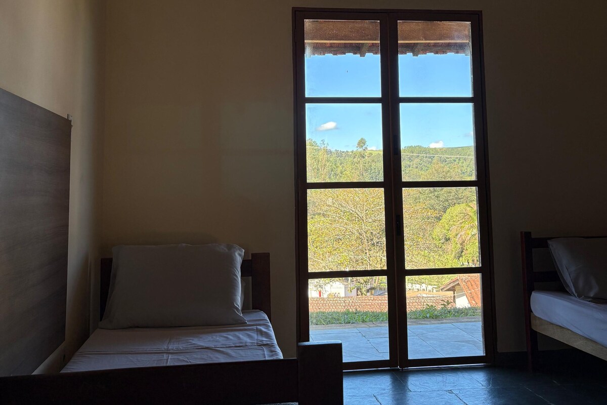 A room with a bed, a bench, and a large window with a view of a landscape.