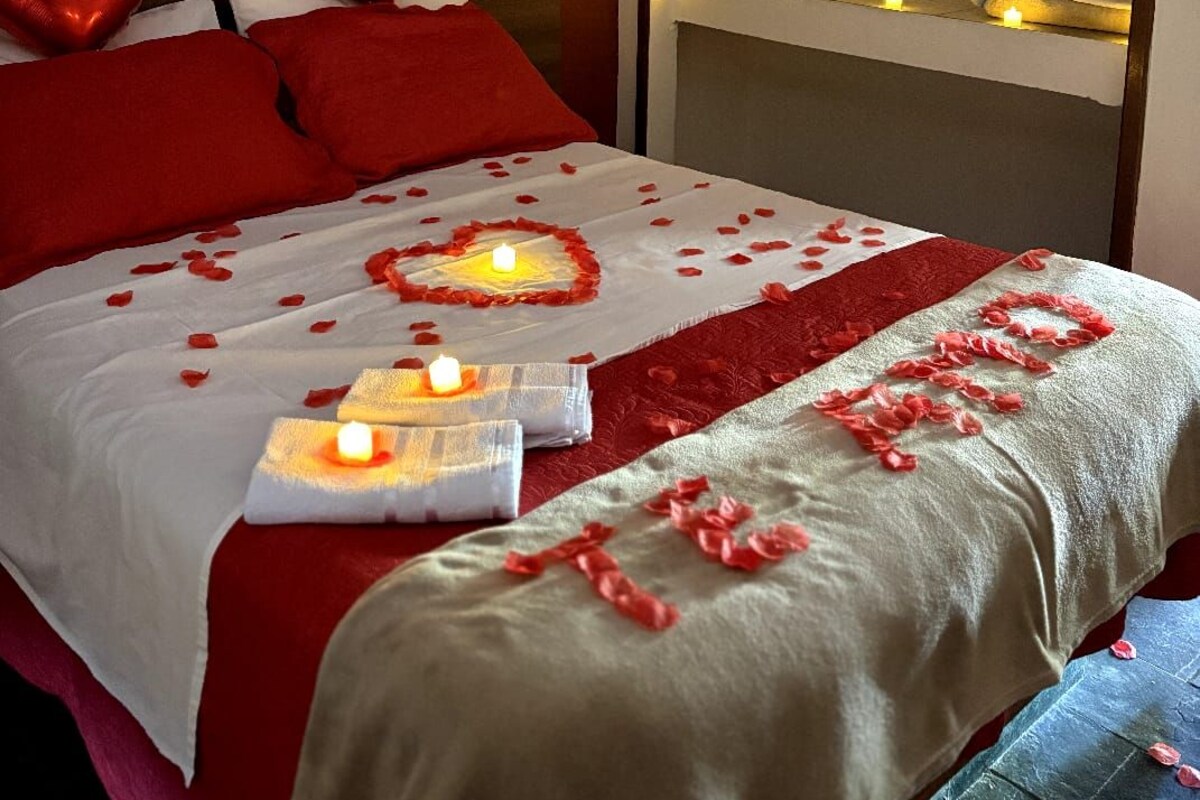 A bed with red pillows, a white bedspread, and rose petals scattered across it.