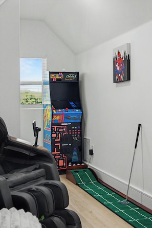 Une pièce avec une console de jeux, une moquette verte et une fenêtre avec des stores.