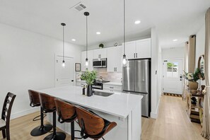 A modern kitchen with a central island, stainless steel appliances, and a dining area with wooden chairs.