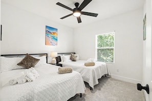 A hotel room with two beds, a ceiling fan, a painting, and a window with blinds.