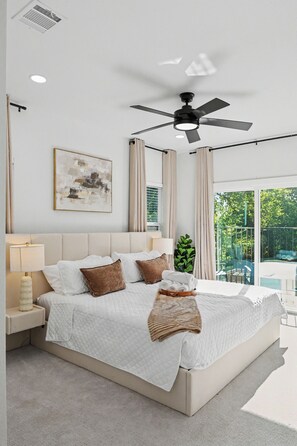 Une chambre moderne avec un grand lit, un ventilateur de plafond et une vue sur un espace extérieur verdoyant.