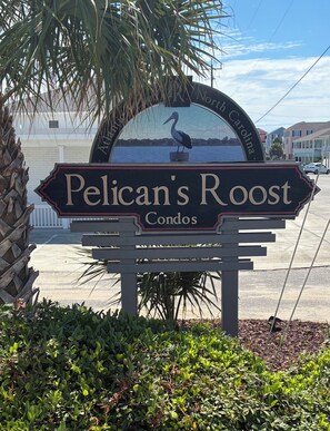 A sign for Pelican's Roost Condos with a bird sculpture and a view of the water.