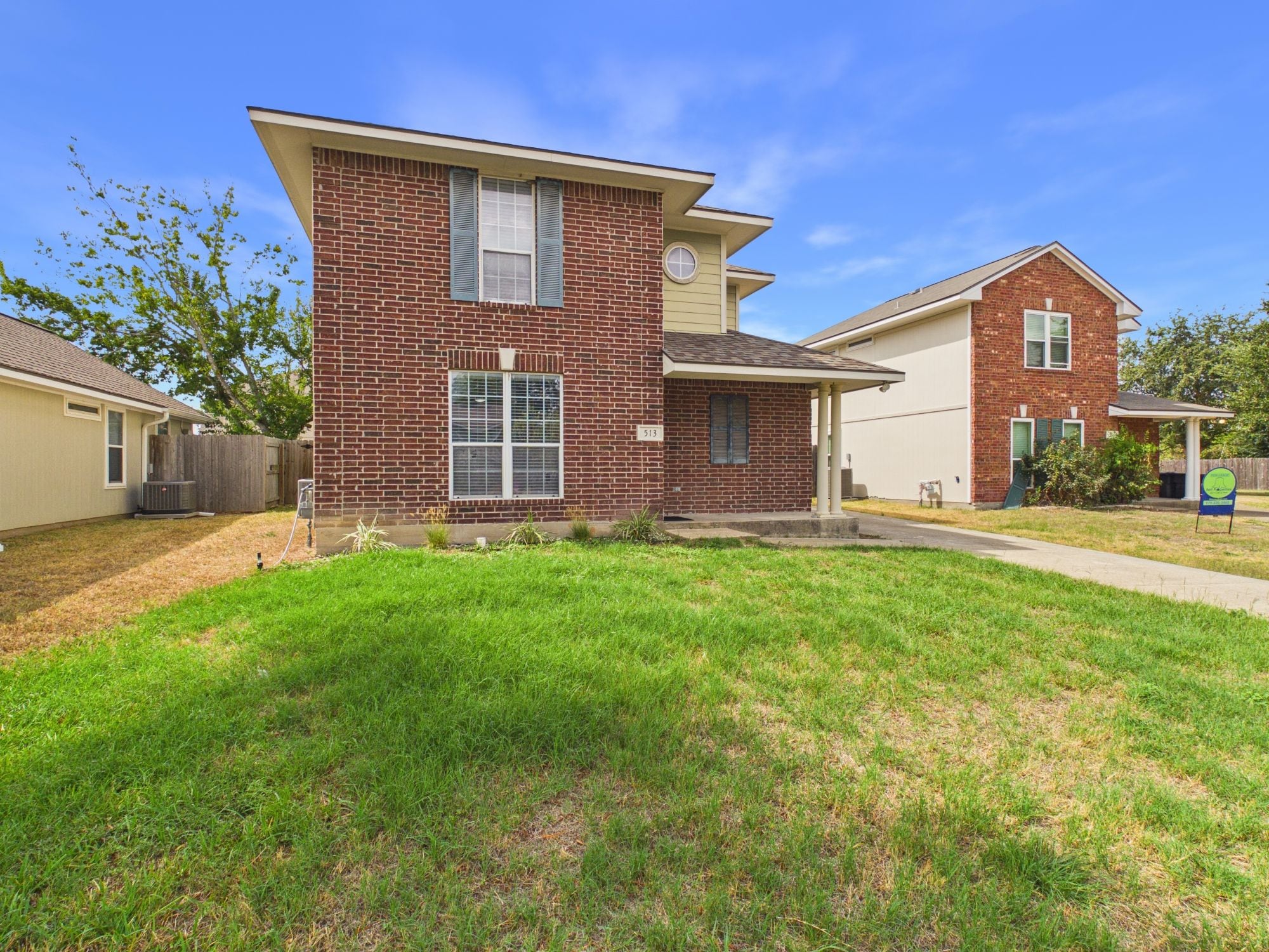 A two-story residential house with a brick facade, a front porch, and a well-maintained lawn.