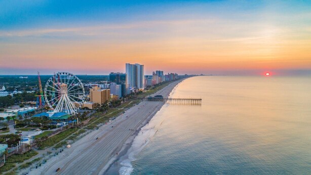 Eine Küstenstadtlandschaft mit einem markanten Riesenrad, Wolkenkratzern und einem Strand.