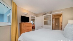 Quarto de hotel com uma cama, uma televisão em uma cômoda de madeira, um guarda-roupa e um banheiro com chuveiro e vaso sanitário.