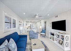 A modern living room with a blue sofa, a coffee table, a TV, and a white entertainment unit. - Direct Gulf‑Front, 2/2 Corner Condo • Panoramic Beach Views & Steps to the Sand (Sanibel)