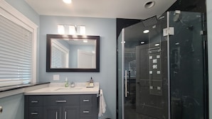 Un baño moderno con tocador oscuro, un espejo grande y una cabina de ducha de cristal.