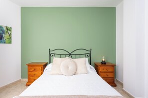 Ein Schlafzimmer mit grüner Wand, einem Metallbettgestell, einer weißen Bettdecke und zwei Nachttischen aus Holz mit Schubladen.