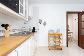 Eine moderne Küche mit Holztresen, Spüle aus Edelstahl und weißen Schränken. Ein kleiner Holzwagen mit Regalen und eine Kaffeemaschine stehen auf der Arbeitsfläche.