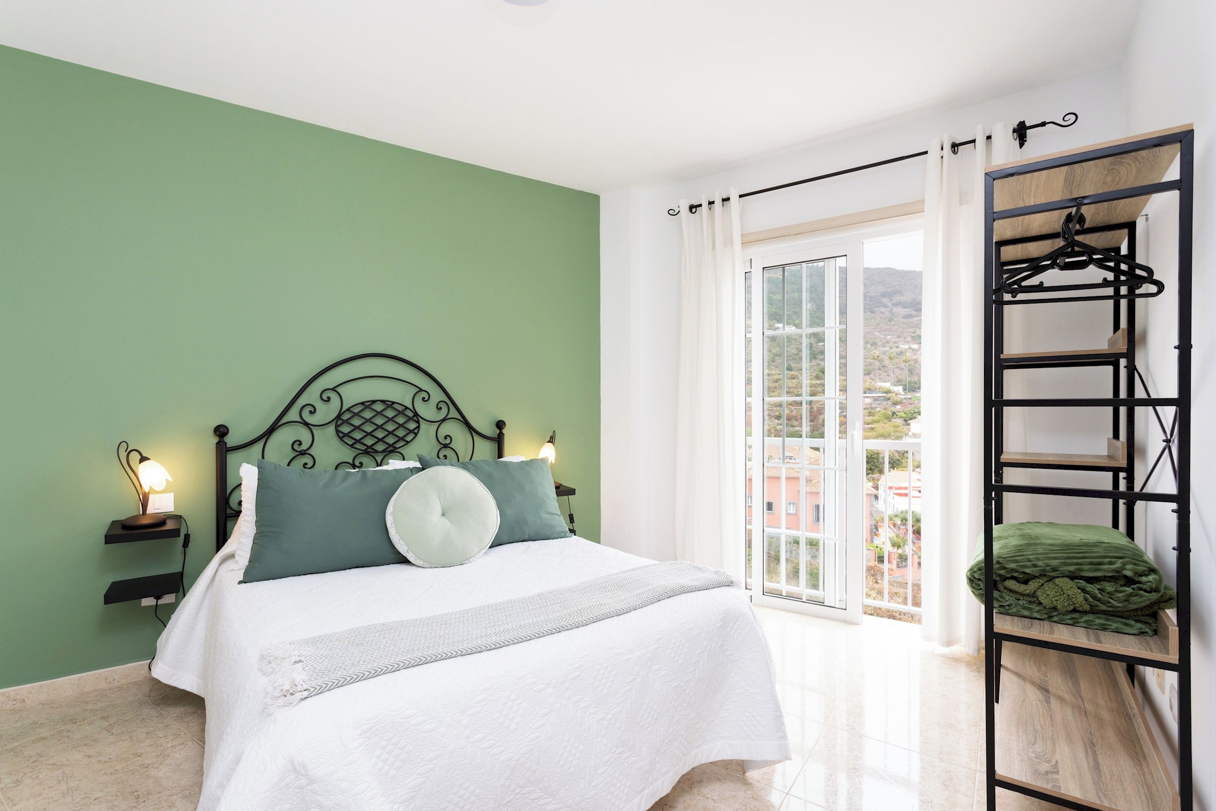 A bedroom with a bed, bedside lamps, a hanging chair, and a view of the outdoors.