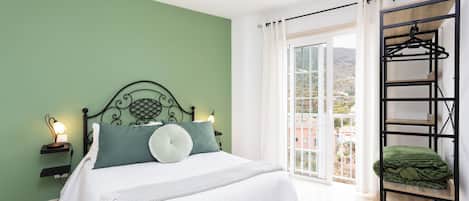 A bedroom with a bed, bedside lamps, a hanging chair, and a view of the outdoors.