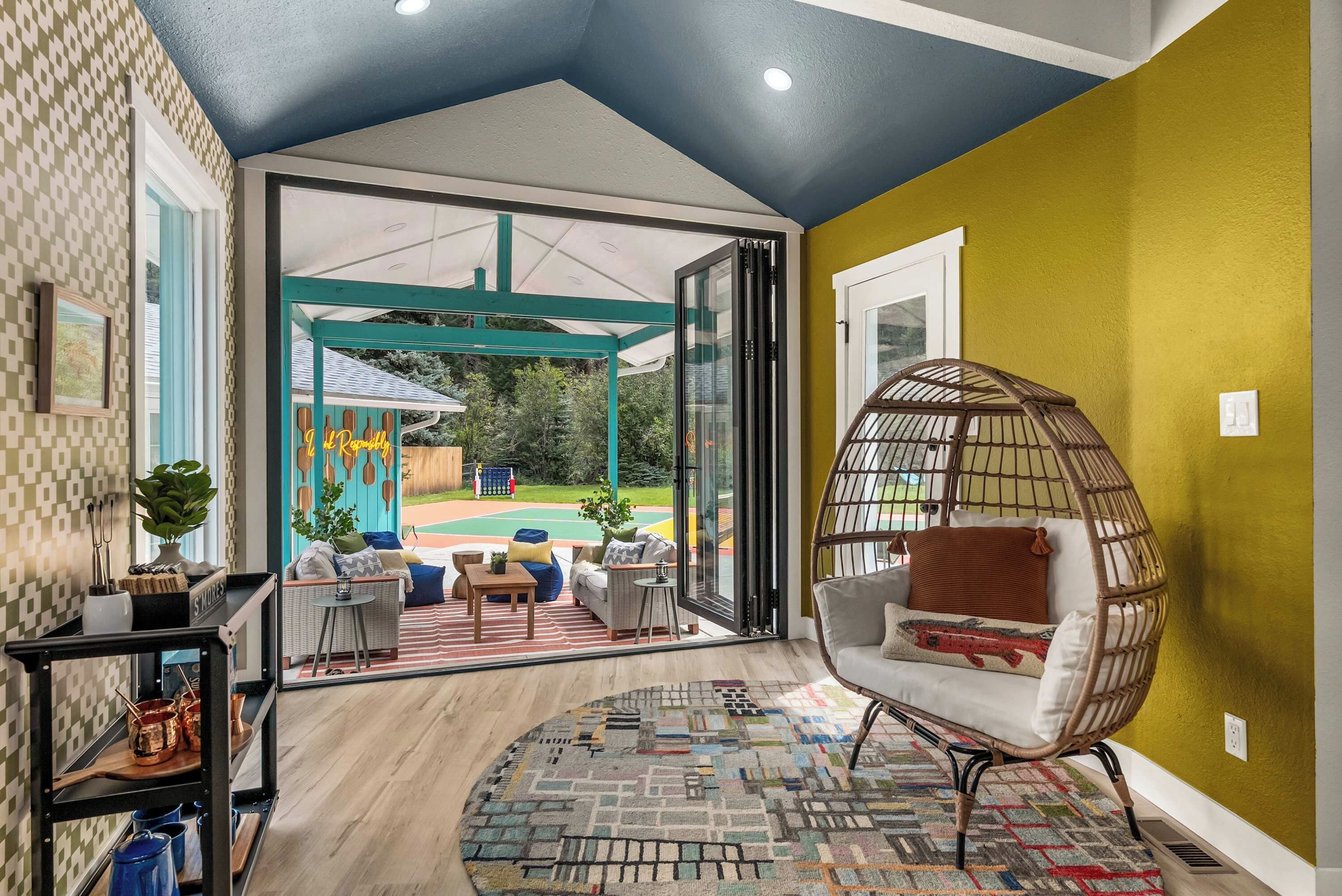 A room with a large glass door leading to an outdoor area, a wicker chair, and a patterned rug.