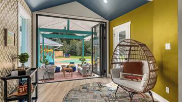 A room with a large glass door leading to an outdoor area, a wicker chair, and a patterned rug.